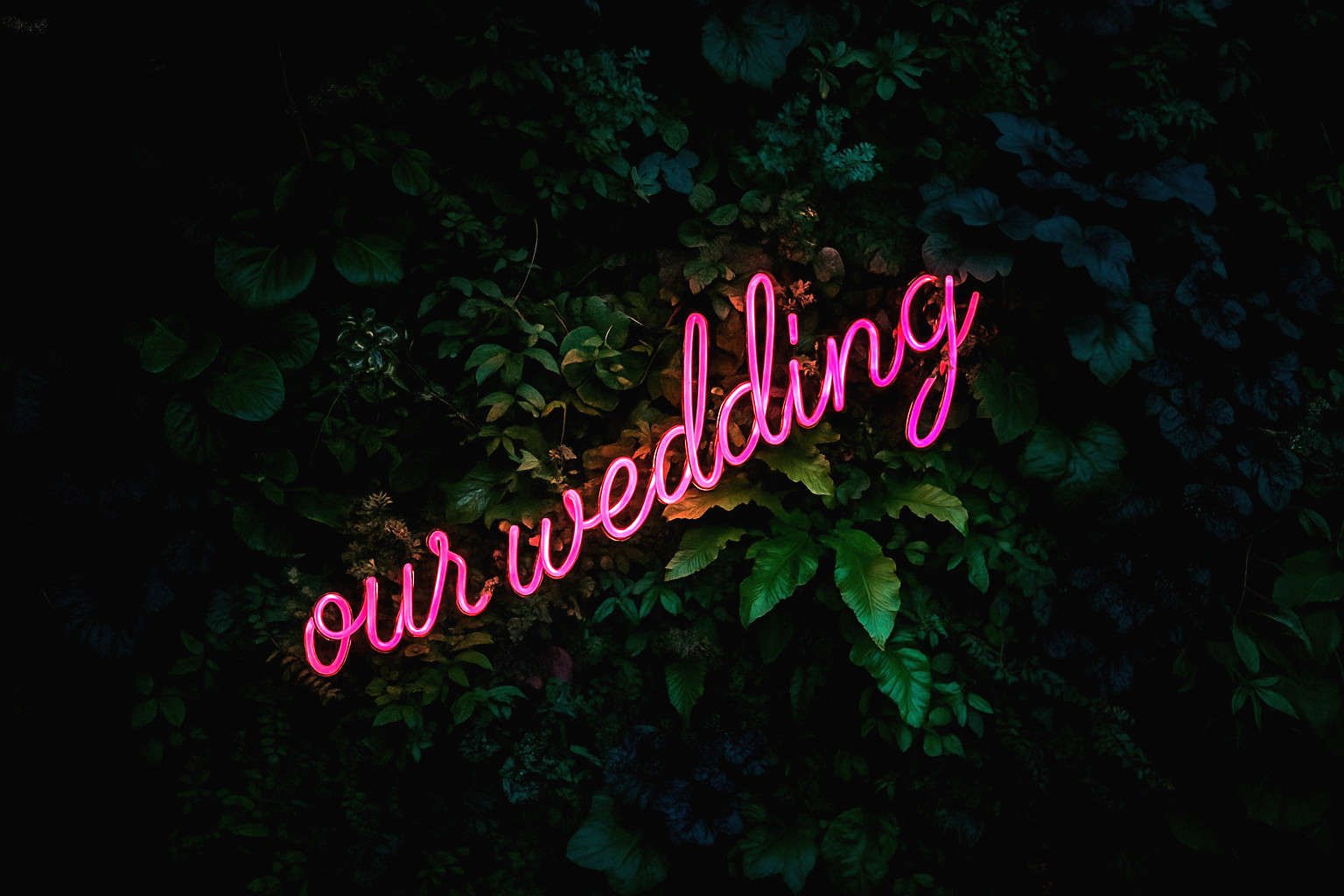 “Our Wedding” Neon Sign – Wedding Decor Inspiration Pink neon sign reading "our wedding" against a lush green foliage wall